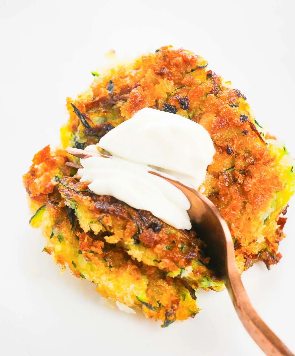 Fork breaking apart a zucchini fritter topped with sour cream