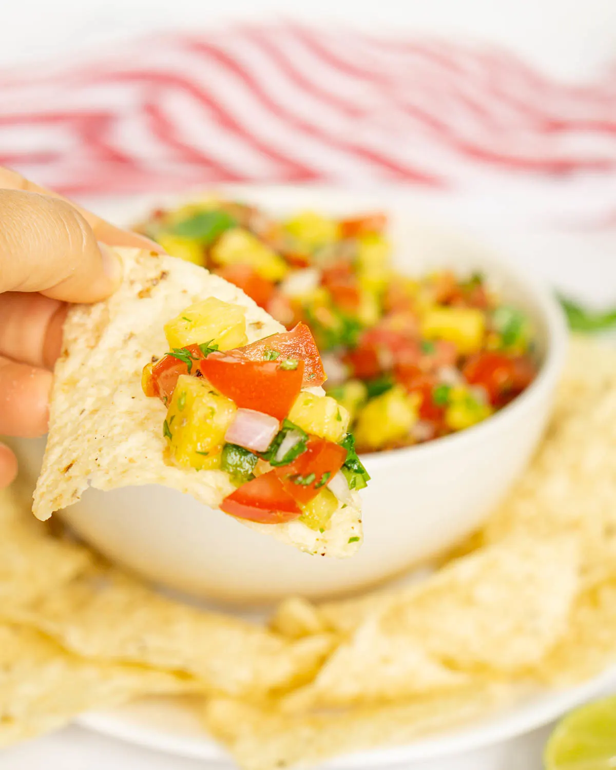 Hand holding tortilla chip with a scoop of pineapple pico de gallo