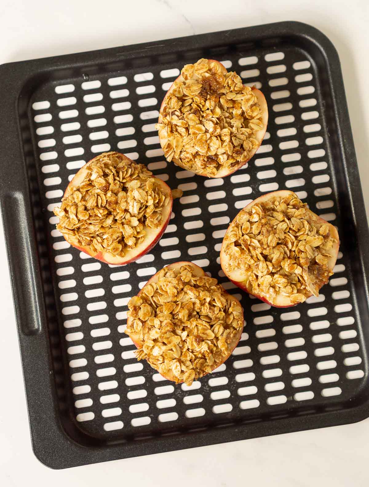 Apple halves stuffed with cinnamon oat topping on an air fryer tray