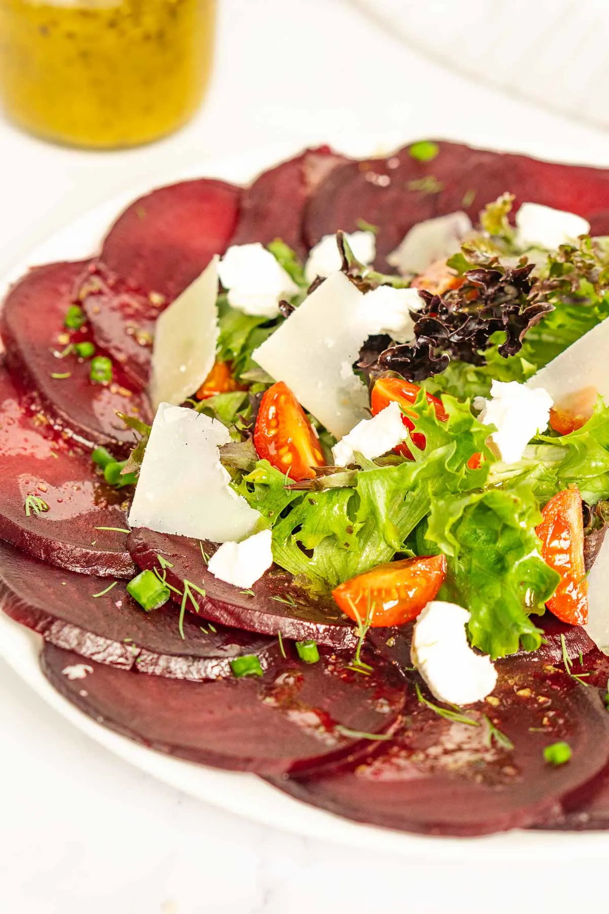 Sliced beet carpaccio topped with salad on a plate