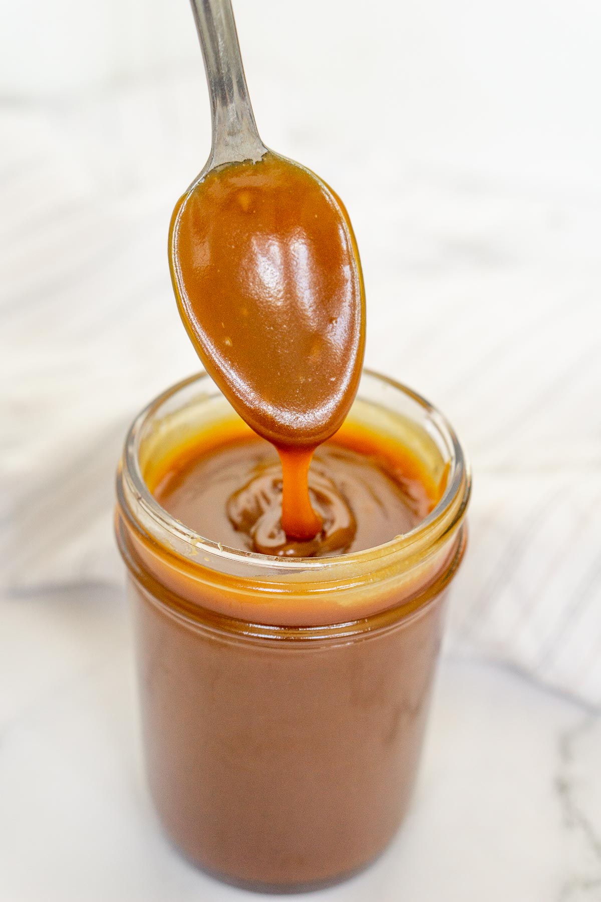 Spoon drizzling bourbon caramel sauce into a jar