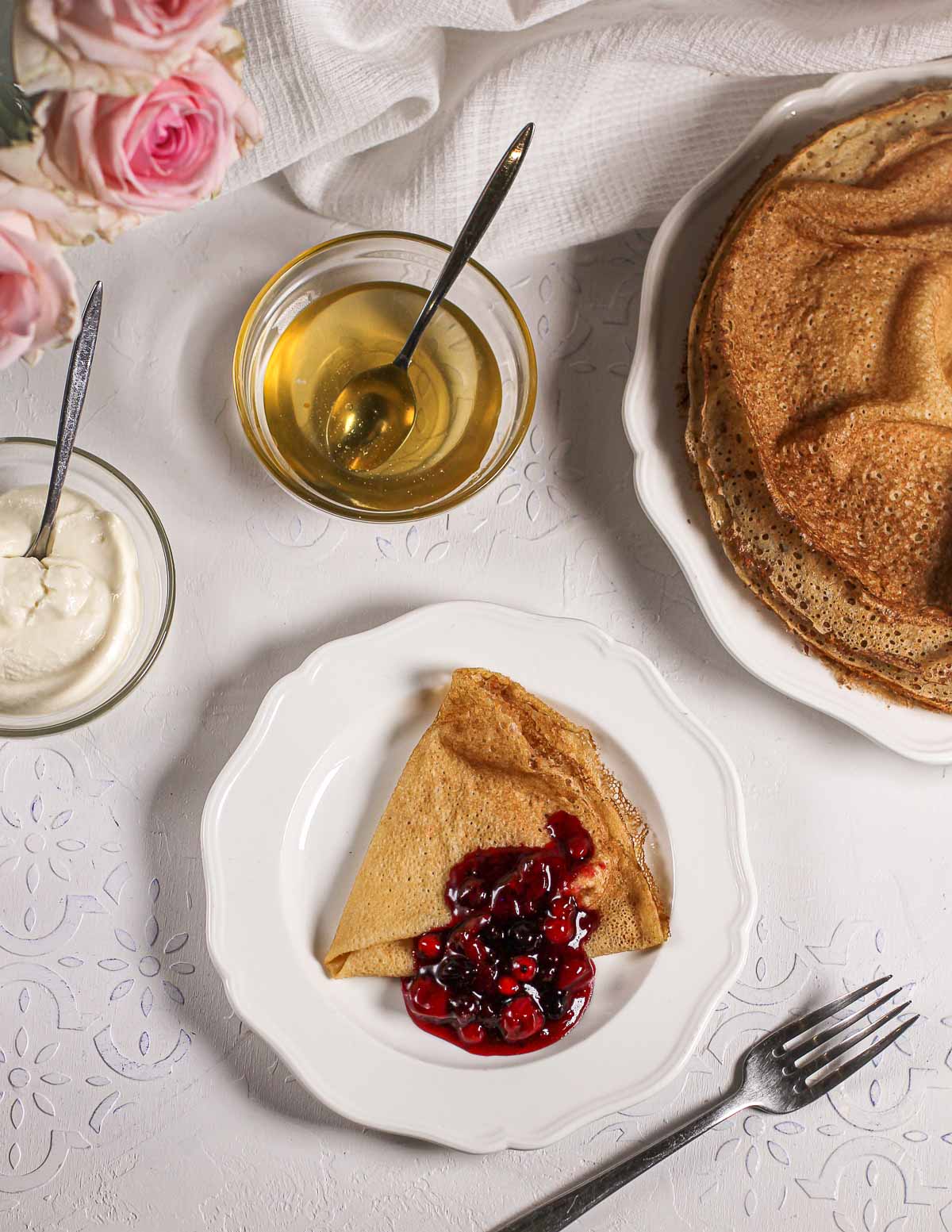 Table with a plate of buttermilk crepes with berry compote and honey