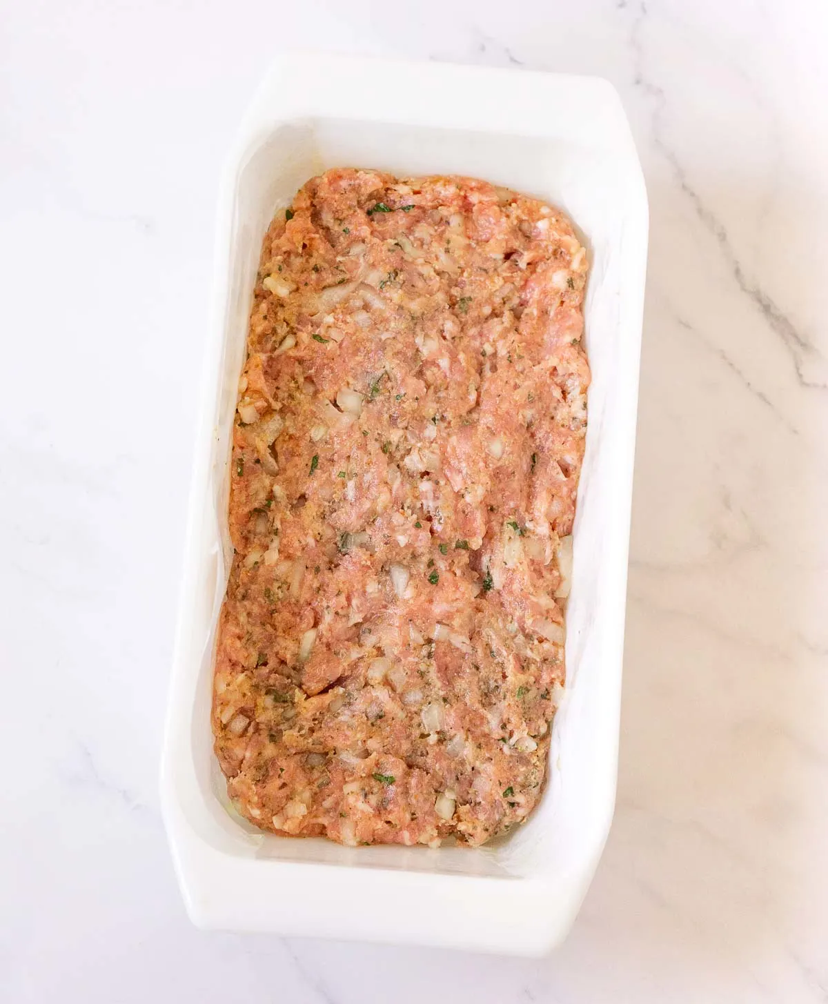 Ground pork meatloaf mixture pressed into a loaf pan