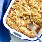 Spoon picking up apple crisp in a baking dish