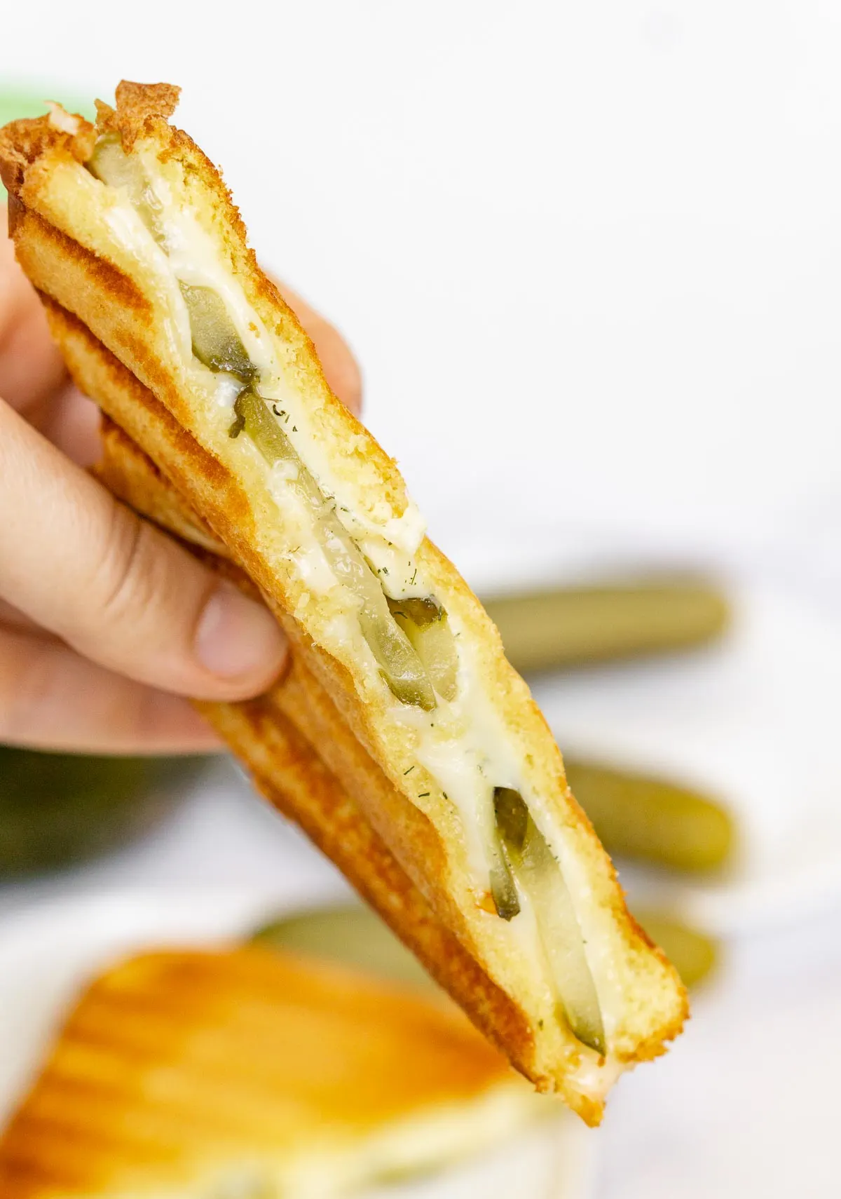 Hand holding grilled cheese sandwich with pickles in it