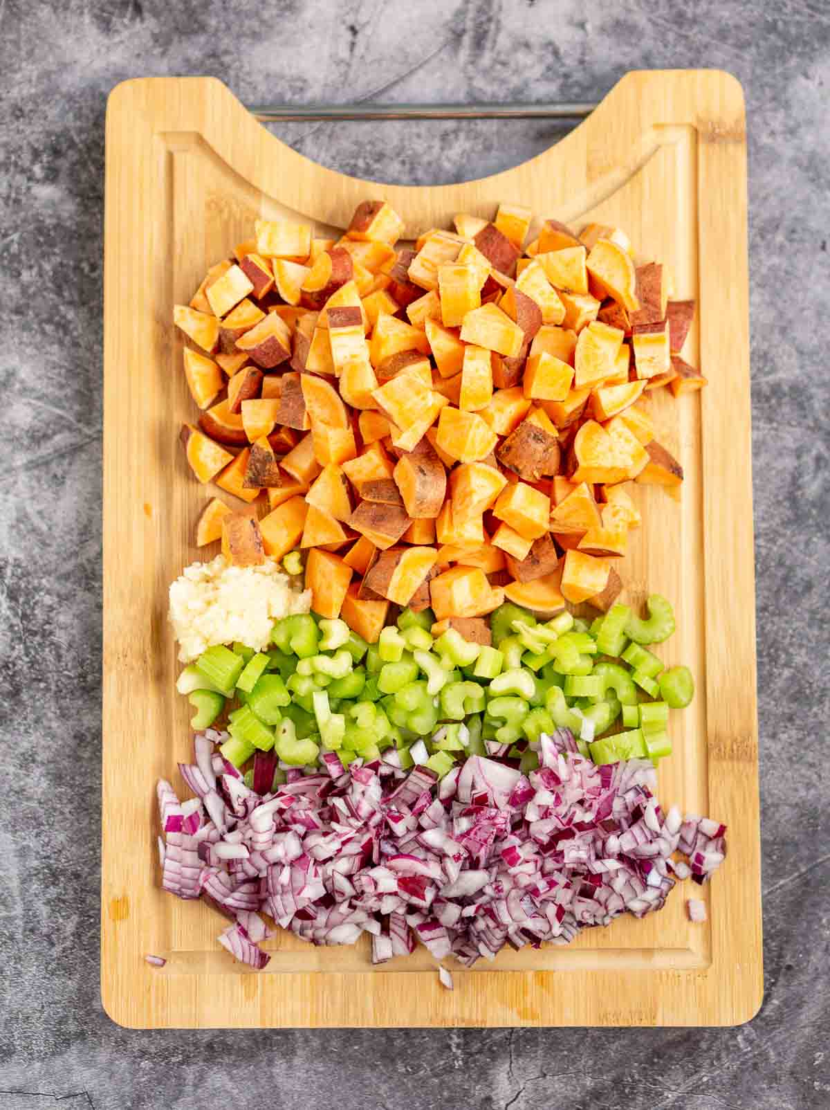 Diced sweet potato, celery, onion, and garlic on a cutting board.