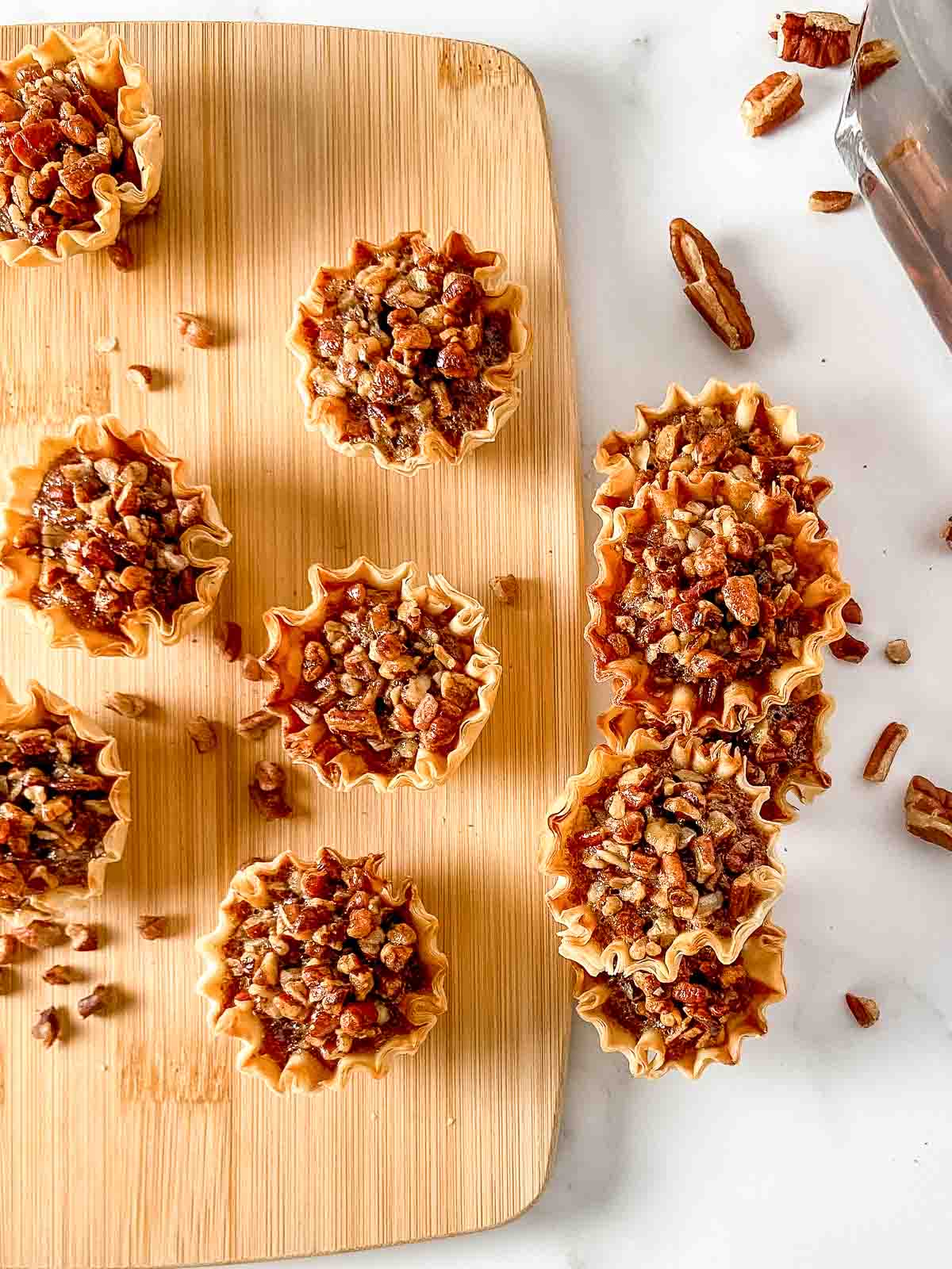 Cutting board with phyllo cup pecan pie bites arranged on it