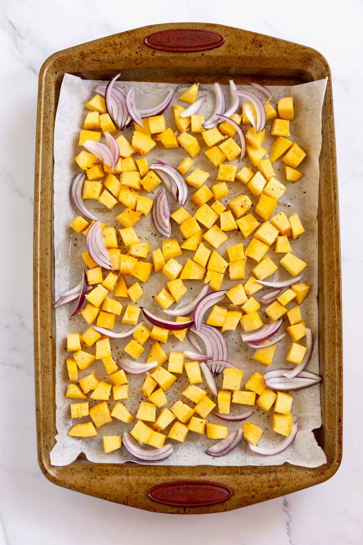Cubed pumpkin and sliced red onion on a baking sheet