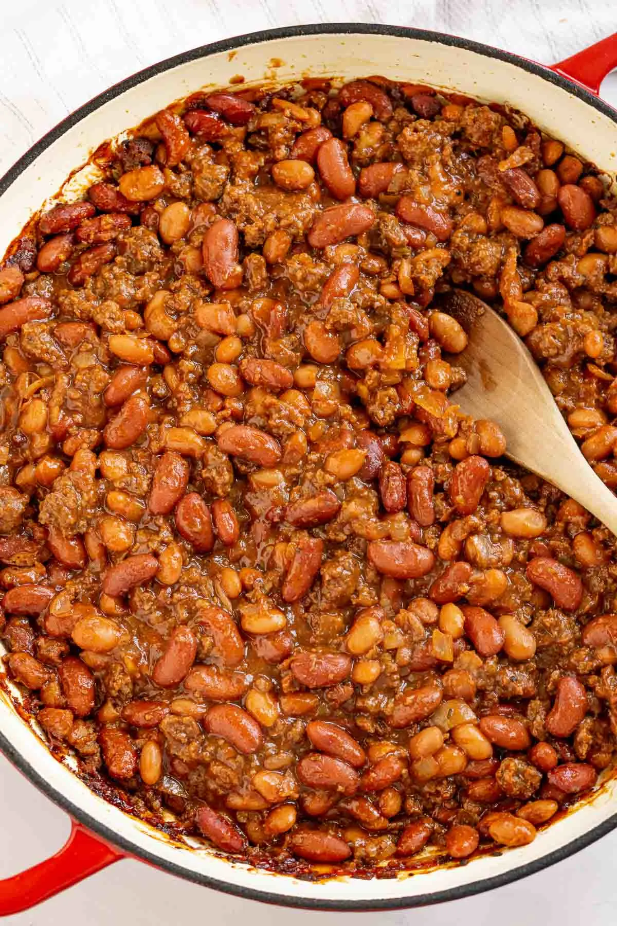 Wooden spoon in a pan of baked beans with ground beef.