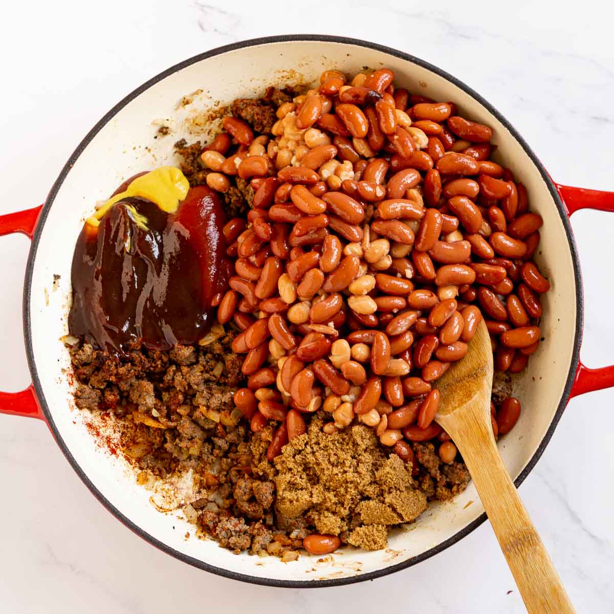 Beans, BBQ sauce, ketchup, and other ingredients added to a pan with ground beef.