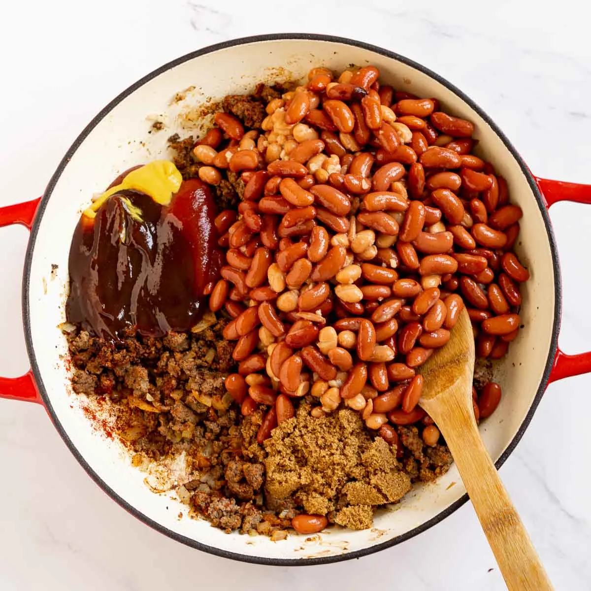 Beans, BBQ sauce, ketchup, and other ingredients added to a pan with ground beef.