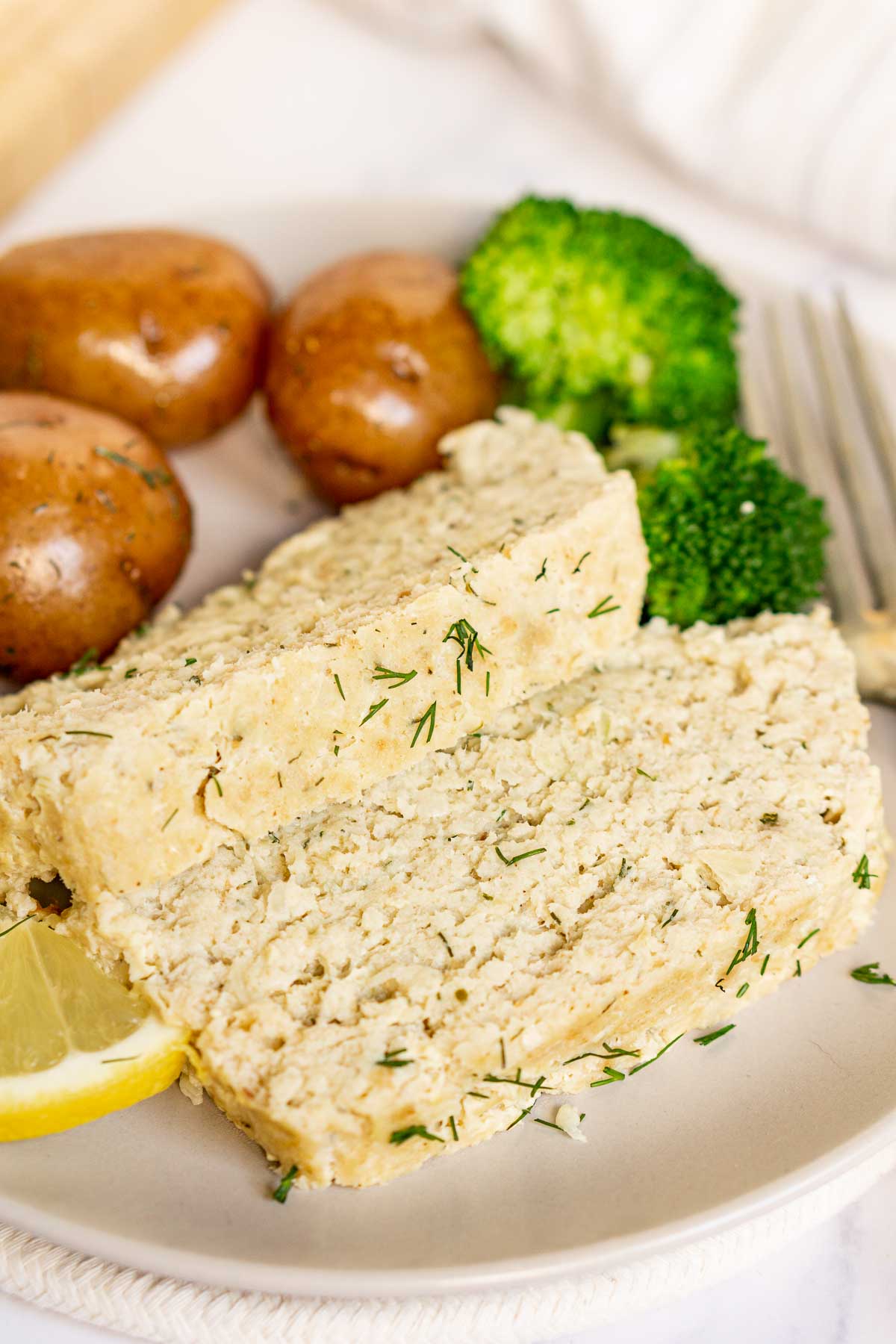 Slices of fish loaf on a plate with potatoes and broccoli