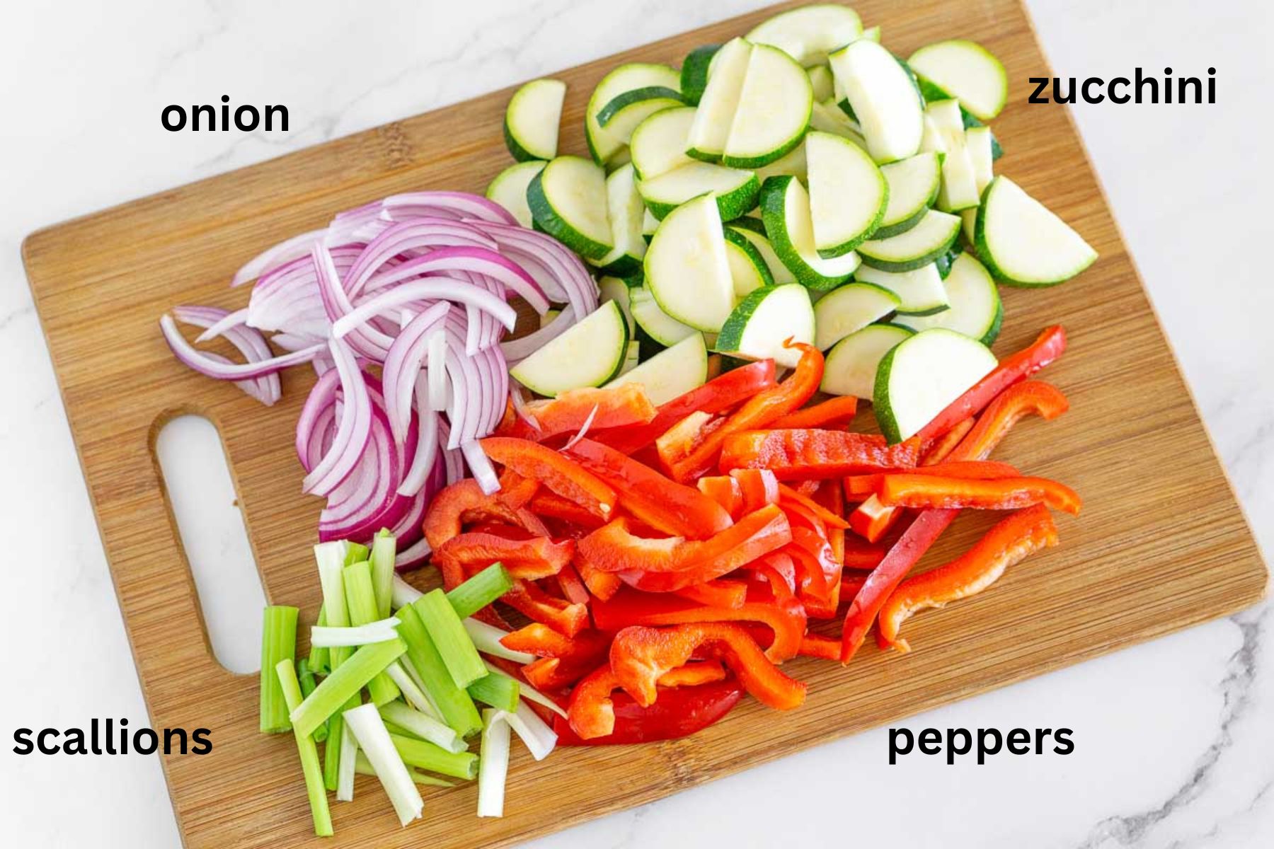 Sliced peppers, onion, zucchini, and scallions on a cutting board.