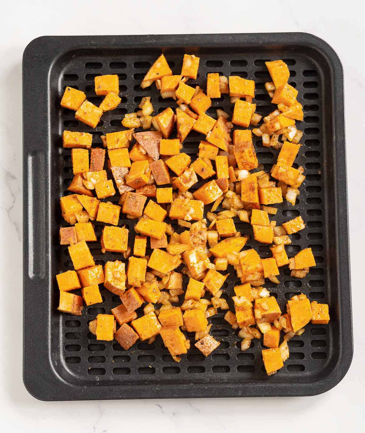 Seasoned cubed sweet potato on an air fryer tray