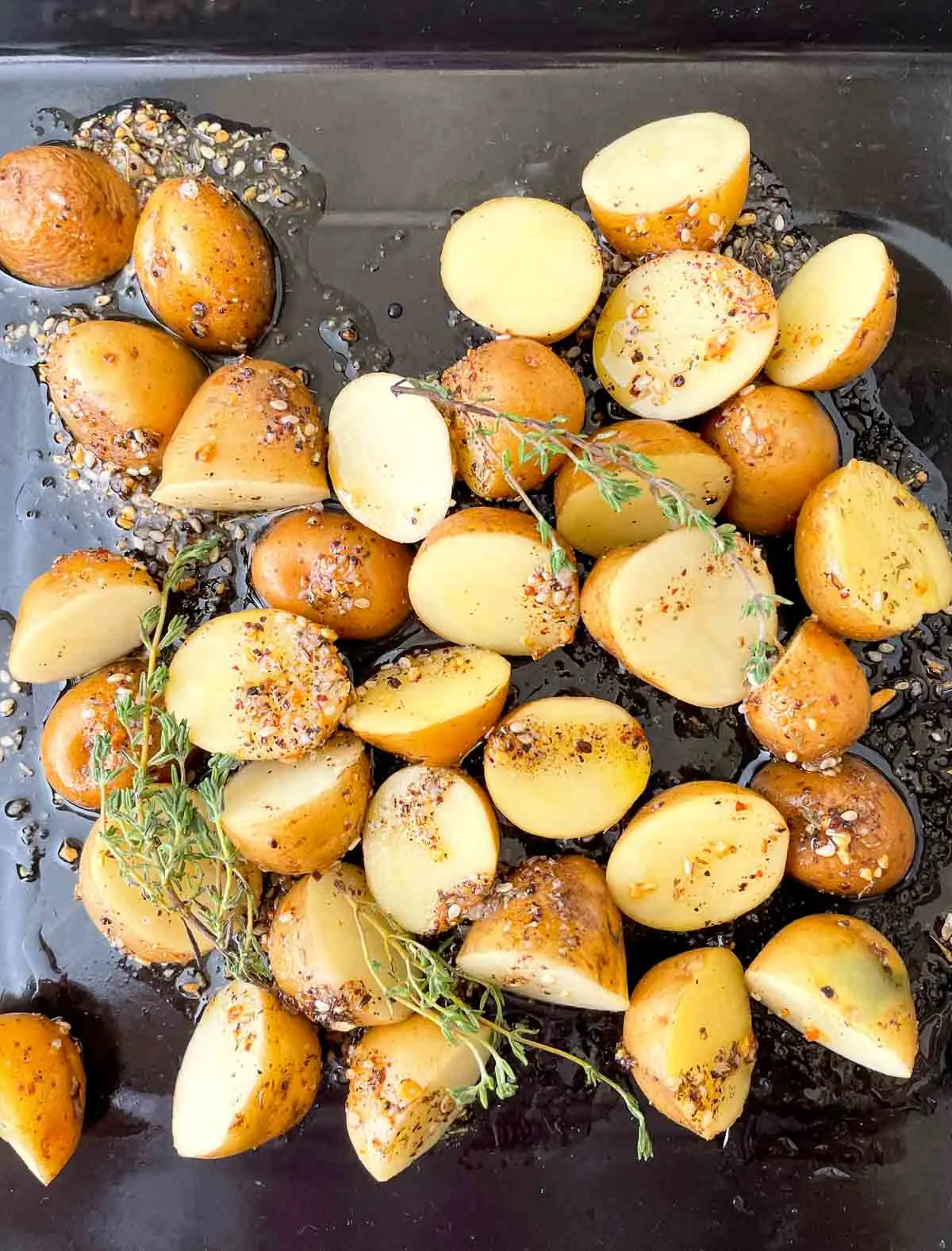 Seasoning young potatoes with zaatar and olive oil on a baking sheet