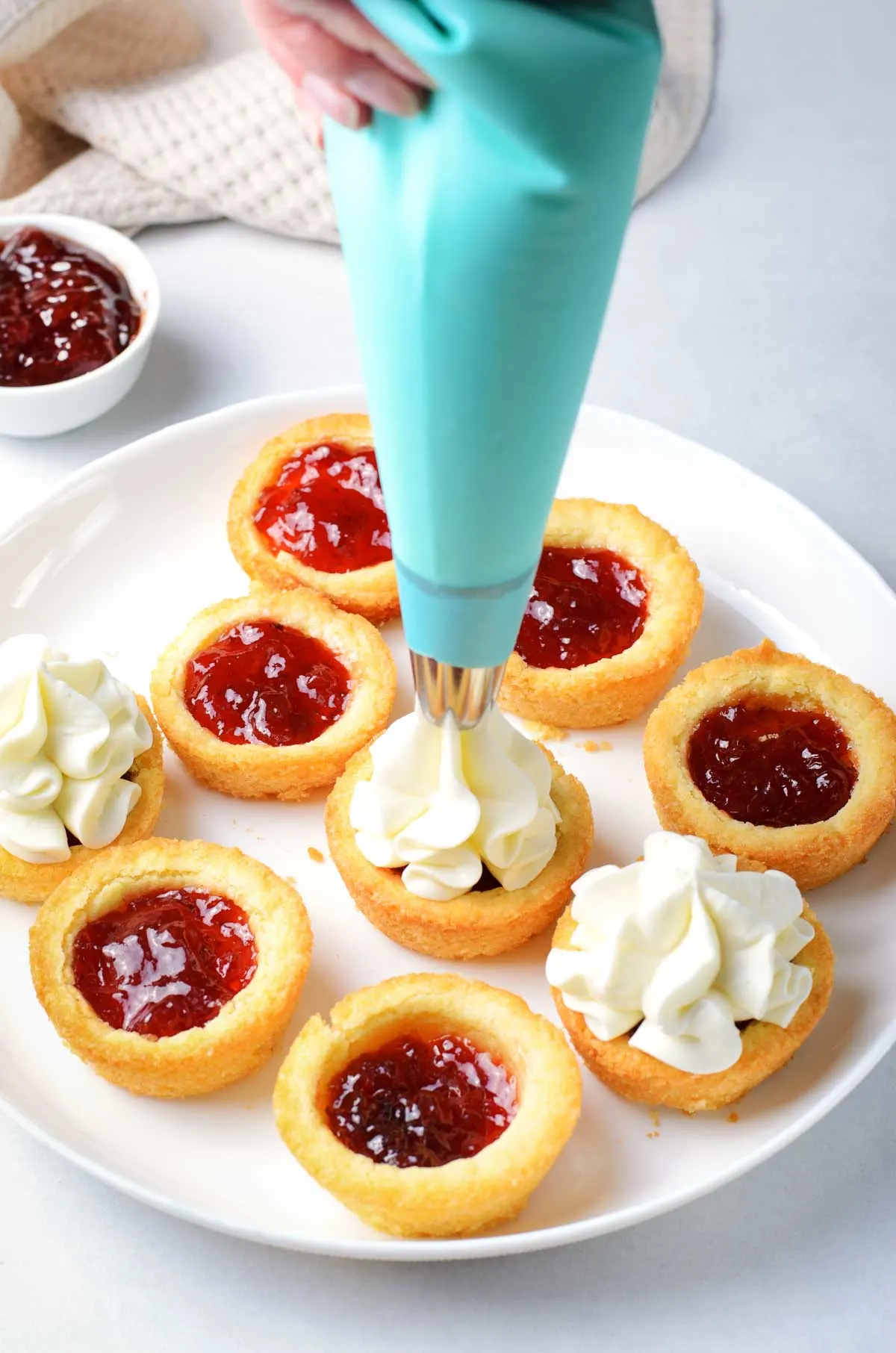 Piping cheesecake filling on a sugar cookie cup filled with jam