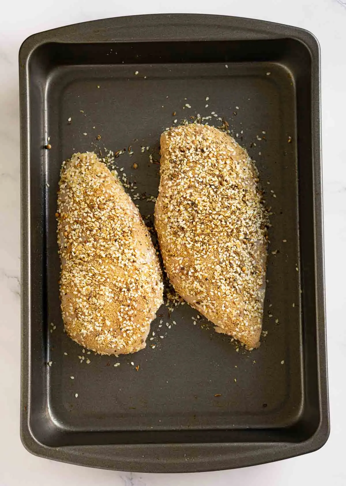 Dukkah coated chicken breast on a baking pan