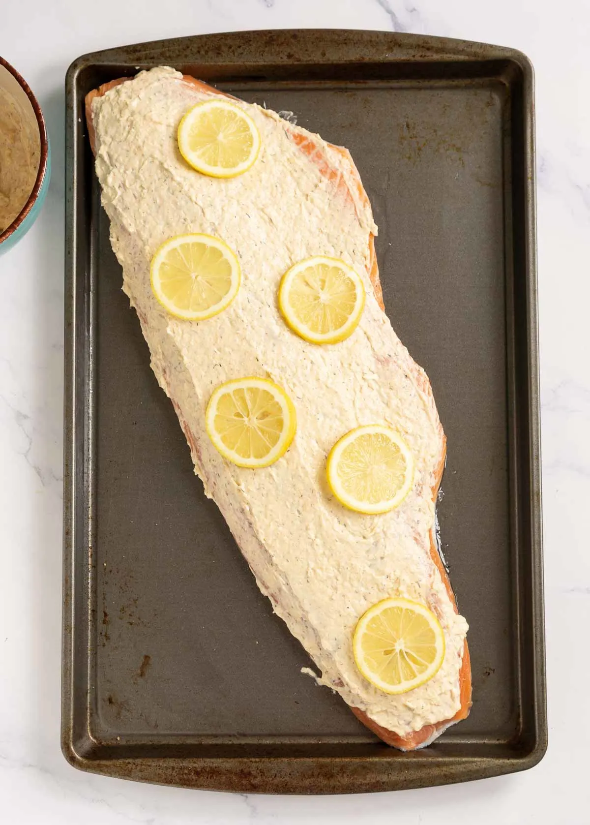 Whole salmon fillet topped with mayo mixture and lemon slices
