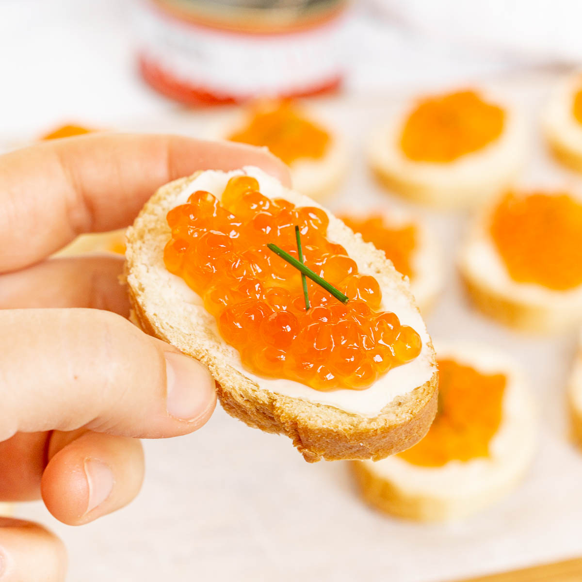 Hand holding a piece of salmon roe crostini