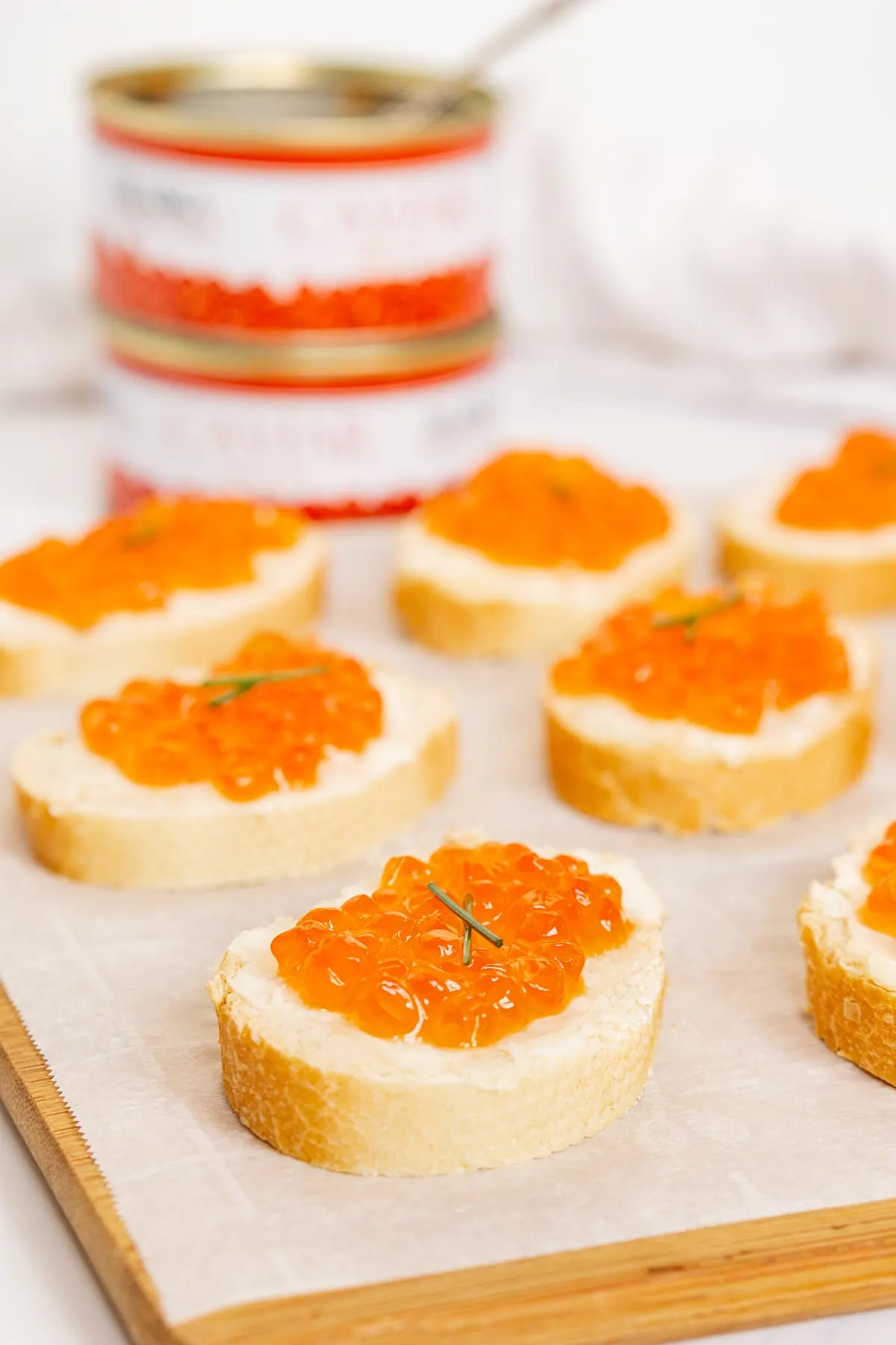 Close up of a red caviar toast with cans of salmon roe in the background