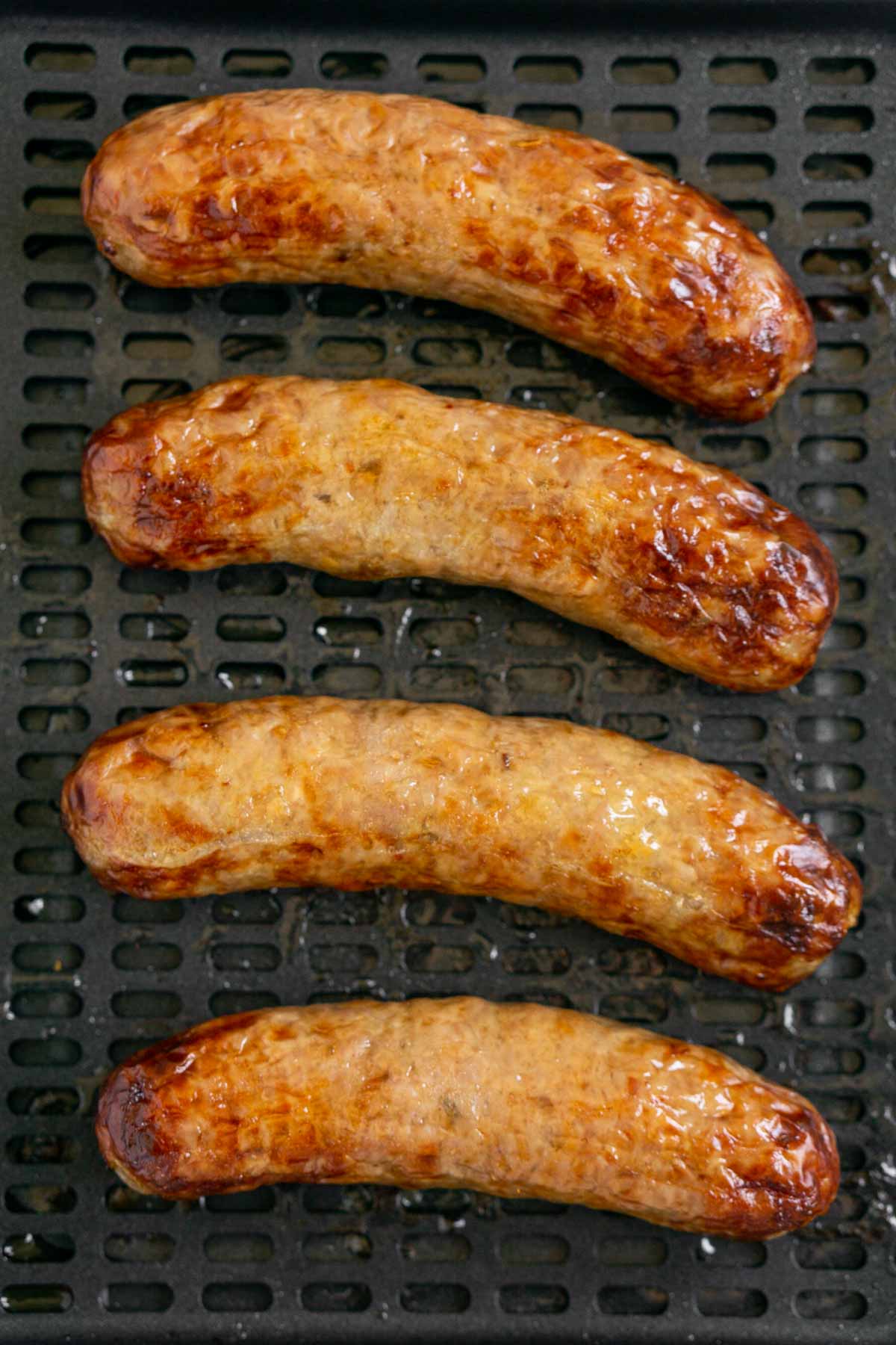 Close up of 4 air fried Italian sausages in an air fryer tray