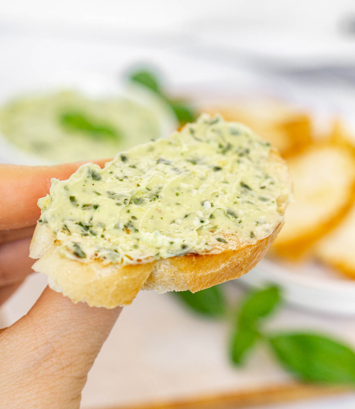 Hand holding baguette slice with pesto butter spread on it