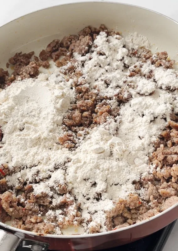 Flour added to a pan with cooked sausage crumbles