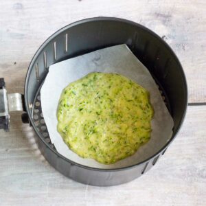 Zucchini batter added to parchment paper in an air fryer basket