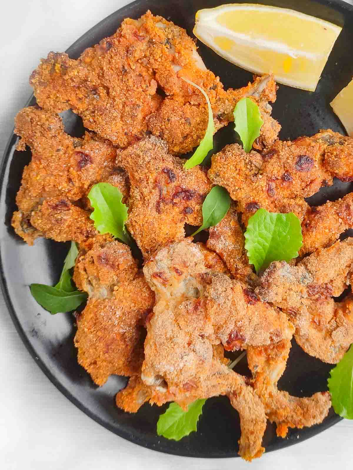 Plate of crispy air fried frog legs with a lemon wedge