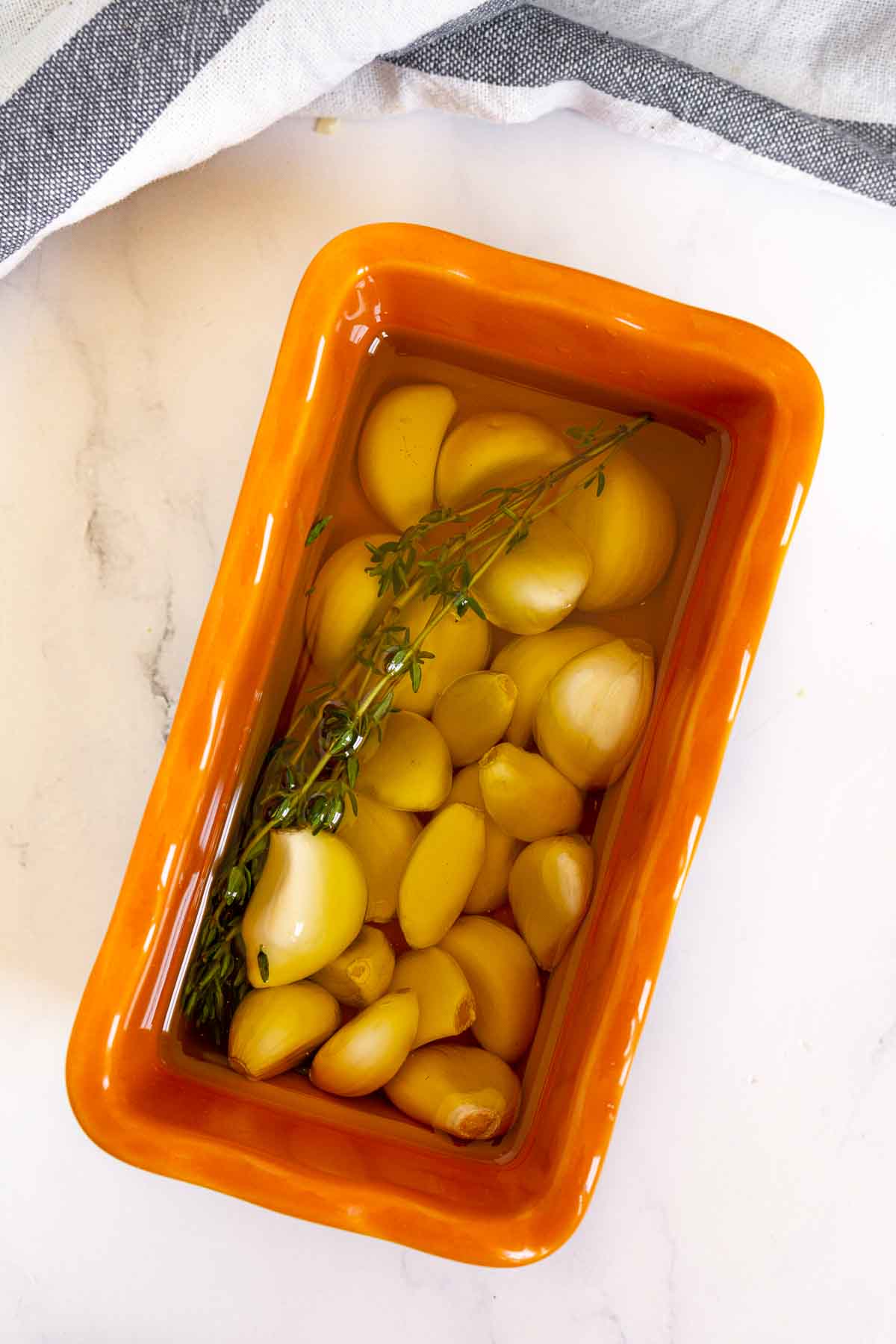 Garlic cloves, olive oil, and a thyme sprig in a small oven-safe container
