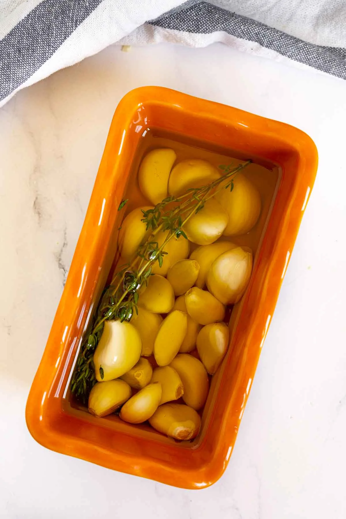 Garlic cloves, olive oil, and a thyme sprig in a small oven-safe container