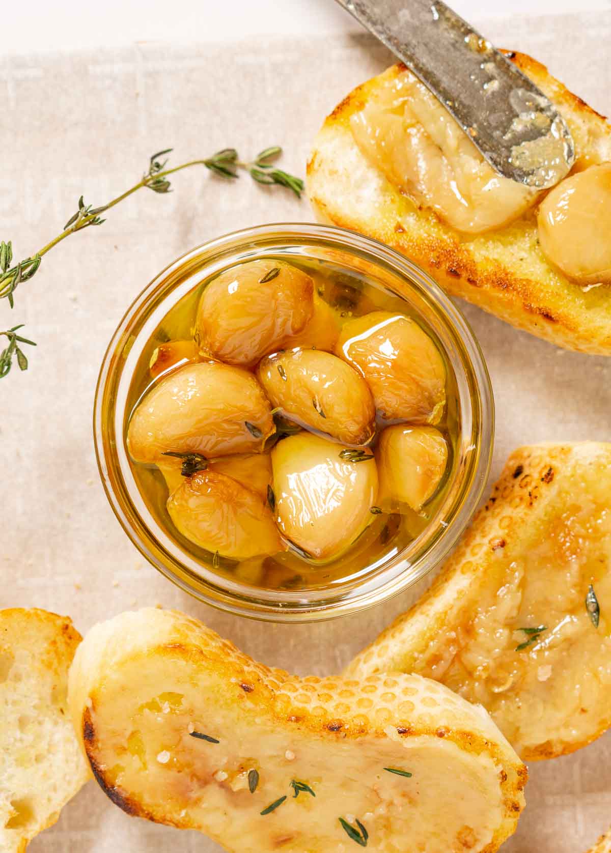 Bowl of roasted garlic confit surrounded by crostini with roasted garlic spread on them