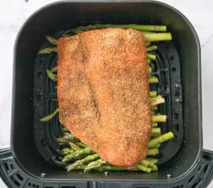 Seasoned salmon on top of asparagus in an air fryer basket