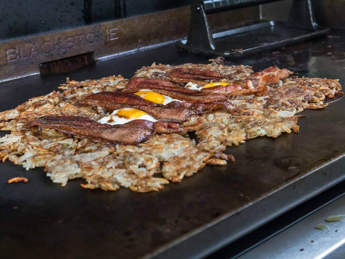 Hash browns with eggs and bacon cooking on a Blackstone griddle