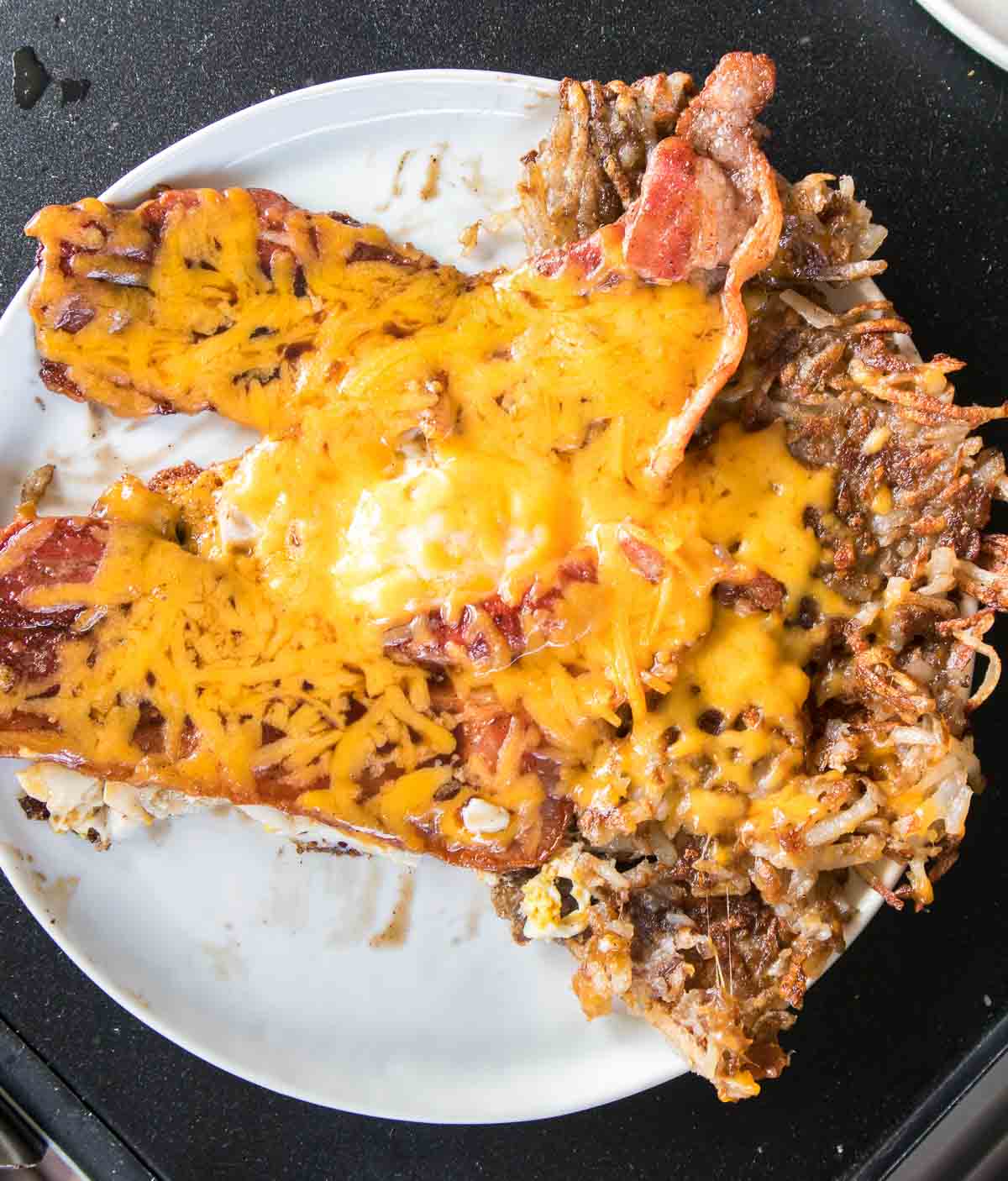 Plate of crispy hash browns topped with bacon, egg, and melted cheese