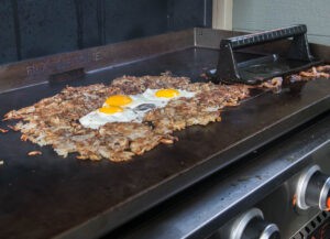 Hash browns on a griddle with eggs cooking in the center