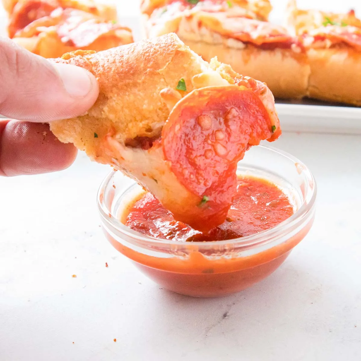 Hand dipping slice of garlic bread pizza into pizza sauce