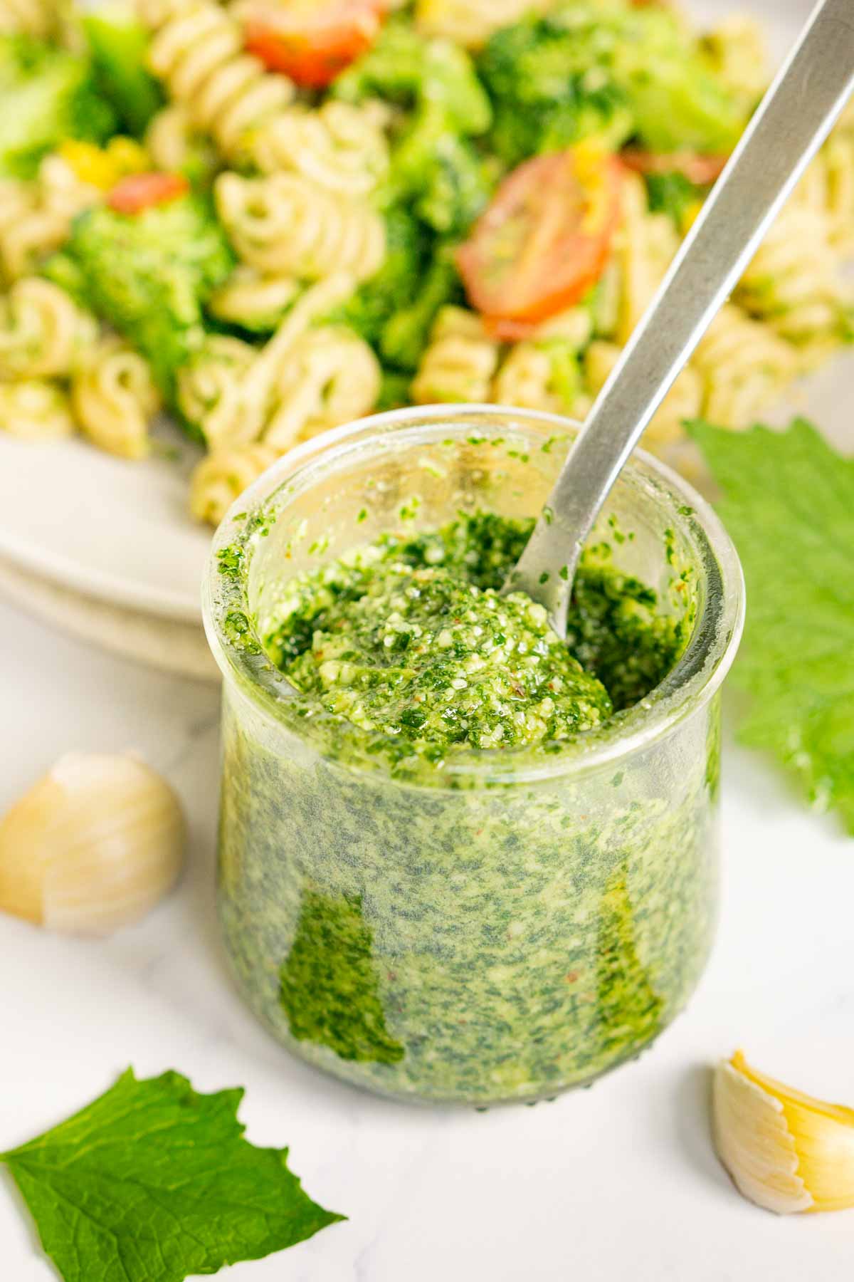 Jar of pesto with a plate of pasta behind it