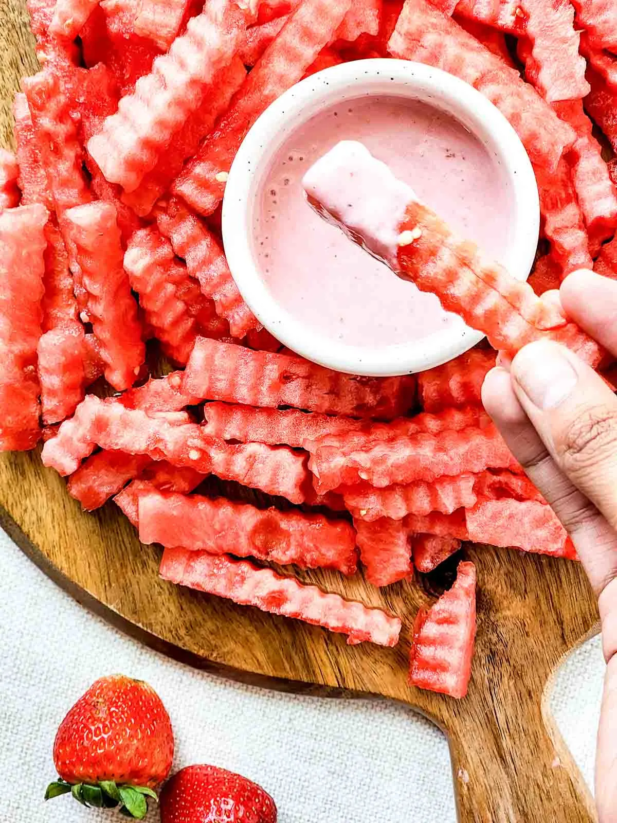 Hand dipping watermelon fry into strawberry yogurt dip