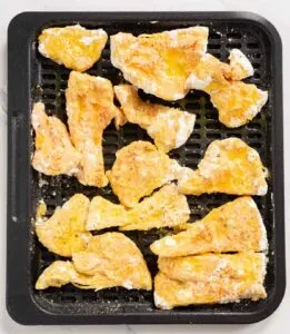Breaded pieces of chicken of the woods mushroom sprayed with oil and on an air fryer tray ready to cook.
