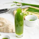 Chive oil in a bottle with chopped fresh chives in the background