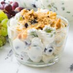 Bowl of grape salad with cream cheese frosting topped with brown sugar and walnuts