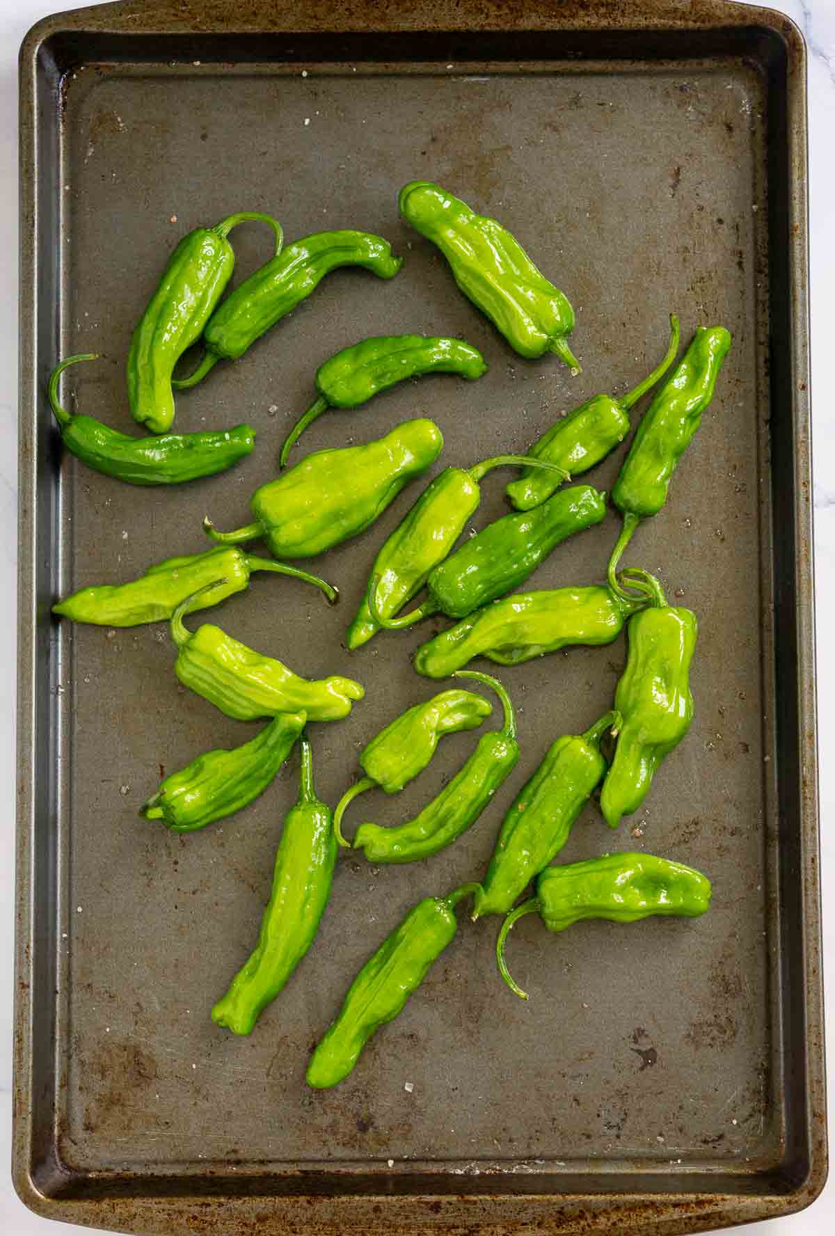 Uncooked shishito peppers on a baking pan tossed with olive oil and sea salt