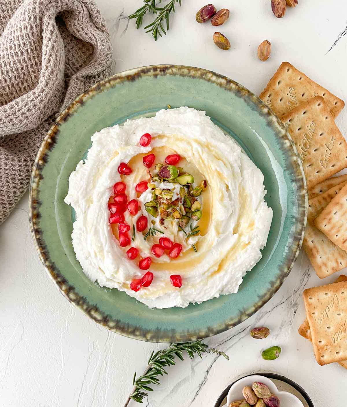 Bowl of whipped goat cheese dip garnished with honey, pistachios, and pomegranate arils