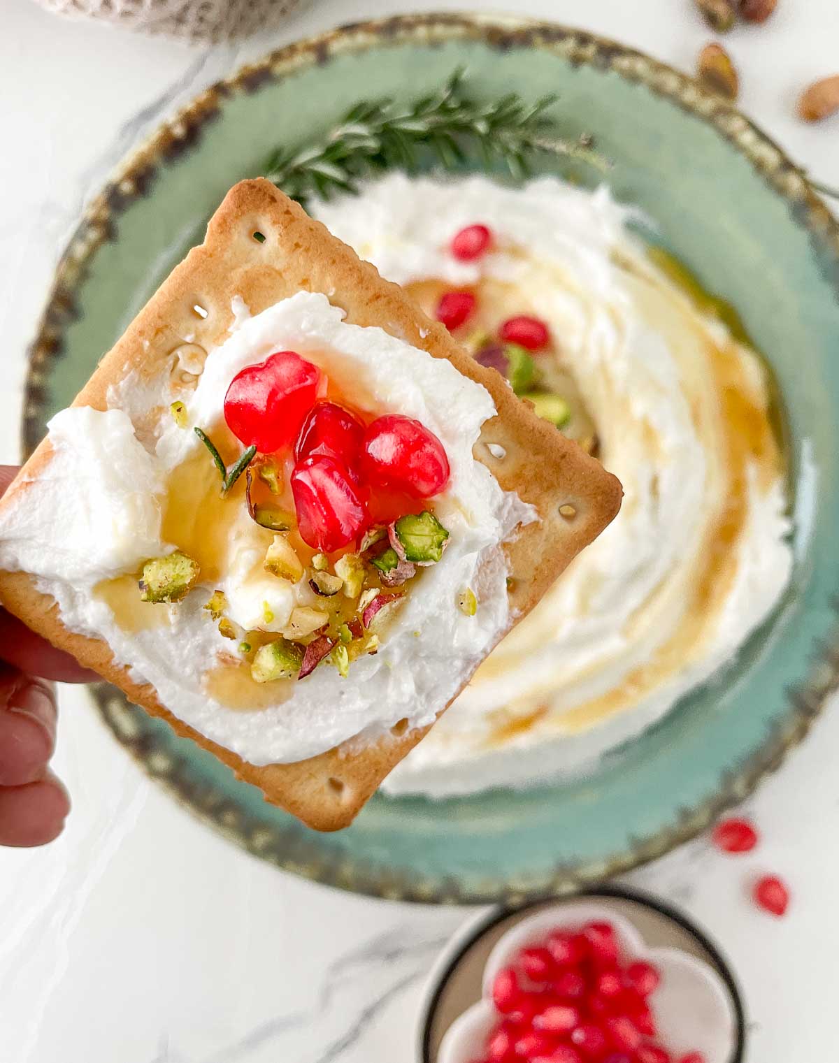 Goat cheese dip with honey, pistachios, and pomegranate on a cracker