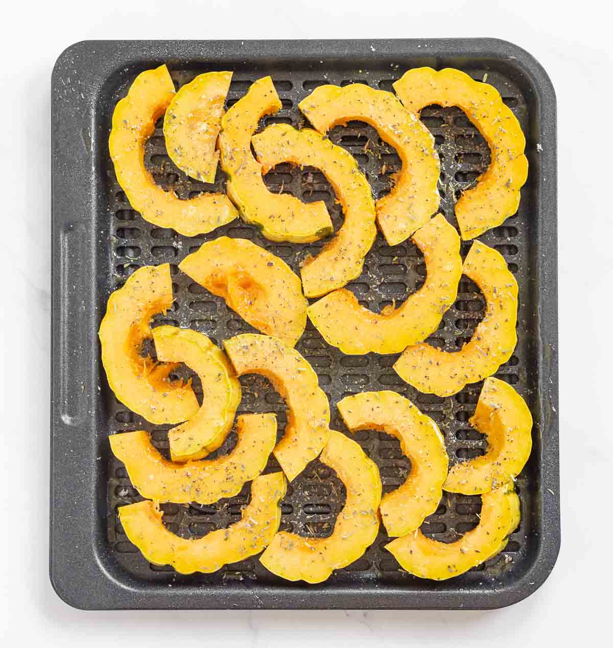 Delicata squash rings in an air fryer tray sprayed with oil and seasoned
