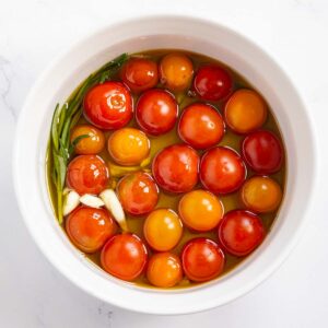 Cherry tomatoes, olive oil, crushed garlic, and fresh rosemary in a baking dish.
