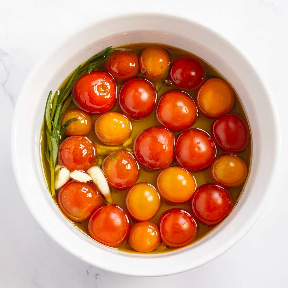 Cherry tomatoes, olive oil, crushed garlic, and fresh rosemary in a baking dish.