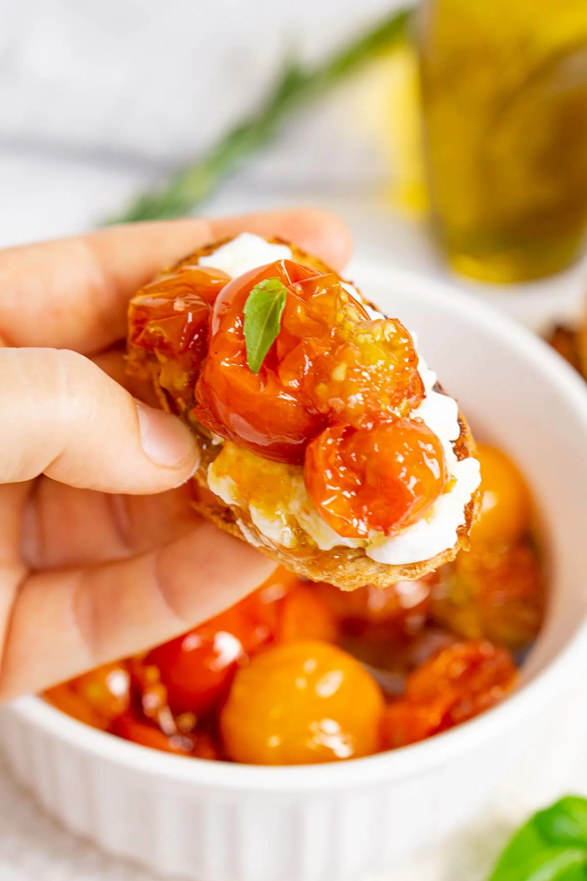 Hand holding cherry tomato confit crostini with burrata