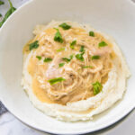 Shredded chicken in creamy gravy cooked in a crock pot served over mashed potatoes